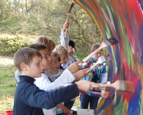 Kinder bemalen mit Pinsel und Acrylfarbe eine Wand im Park