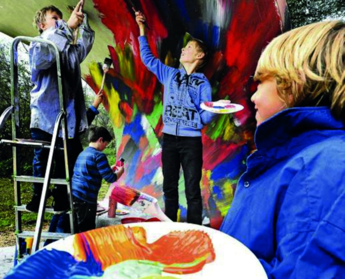 Kinder bemalen mit Pinsel und Acrylfarbe eine Wand im Park